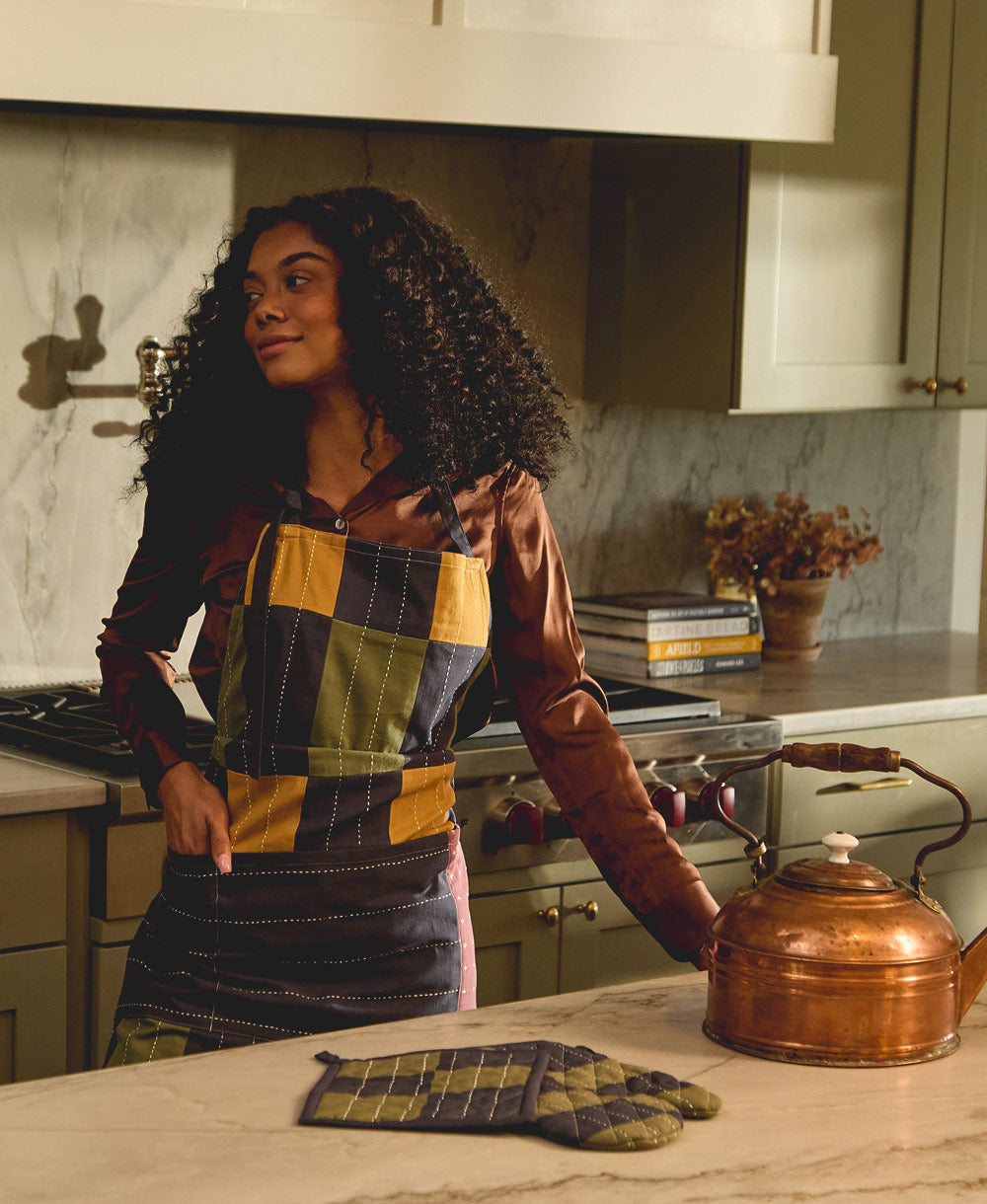 Woman in a kitchen wearing a checkered apron, standing next to a copper kettle