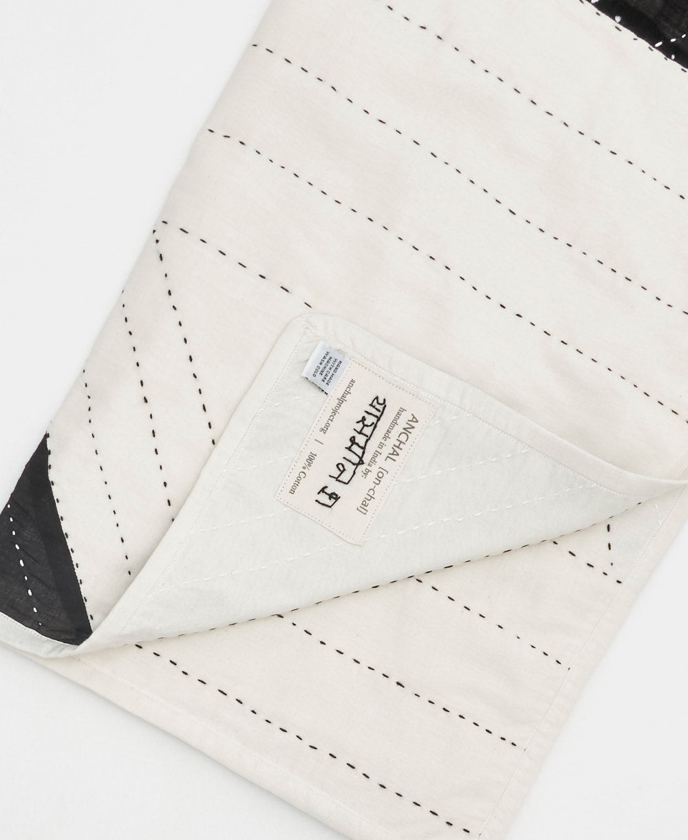 Close-up of a quilt with visible stitching and a brand label on a white background