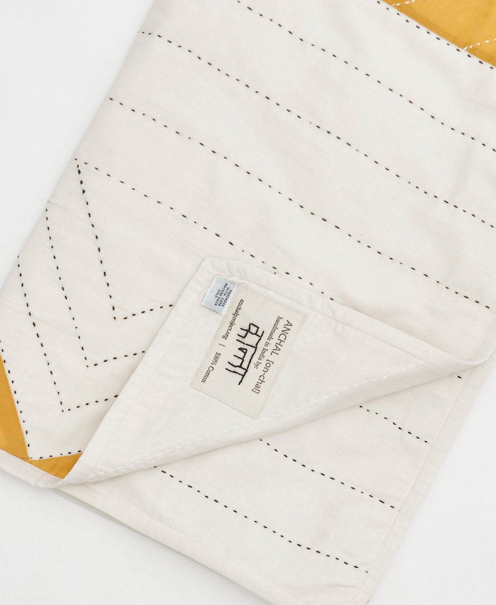 Close-up of a triangle patchwork baby quilt with Anchal's brand label