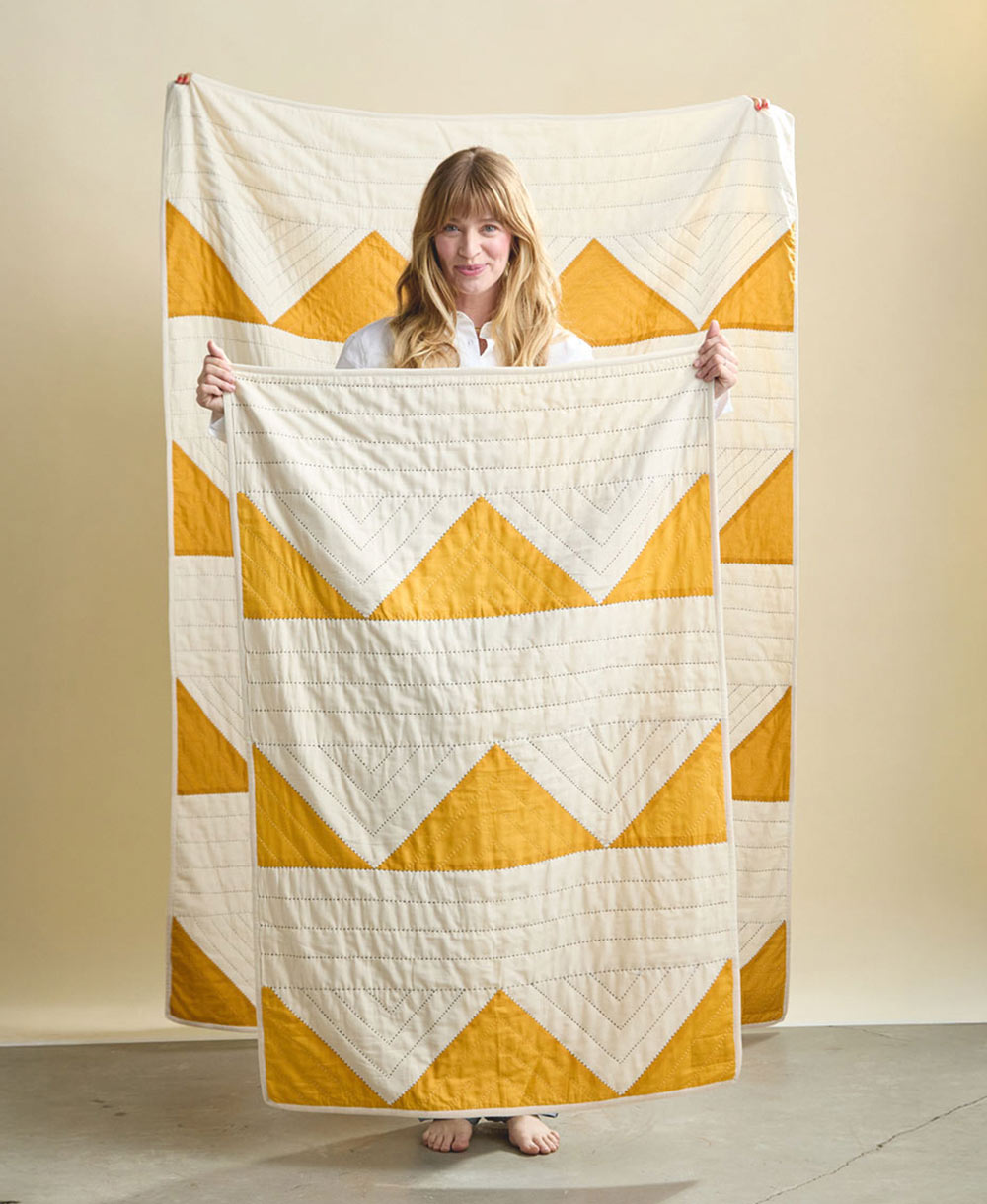 Woman holding a yellow and white chevron patterned quilt against a plain background