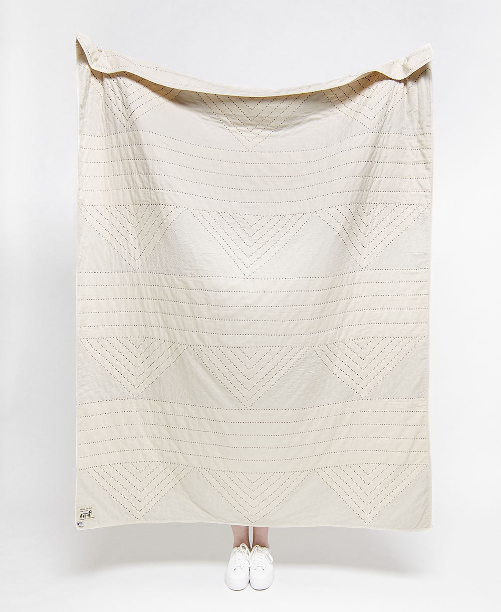 White quilt with geometric pattern draped over a person on a white background
