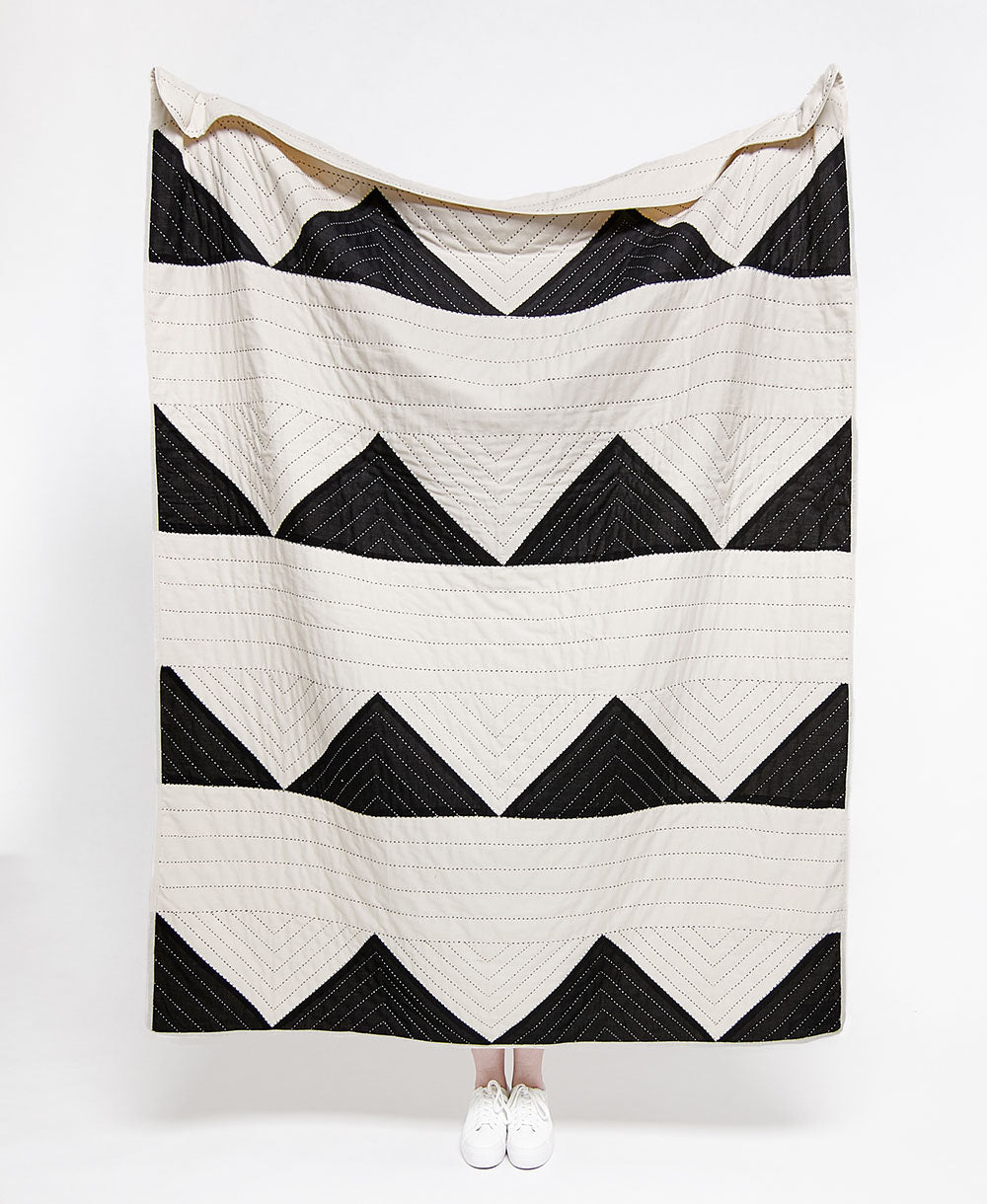 Black and white chevron patterned quilt draped over a person on a white background