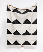 Black and white chevron patterned quilt draped over a person on a white background