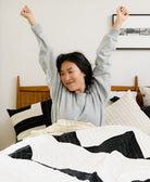 Woman stretching in bed with a cozy black and white patchwork quilt and coordinating pillows