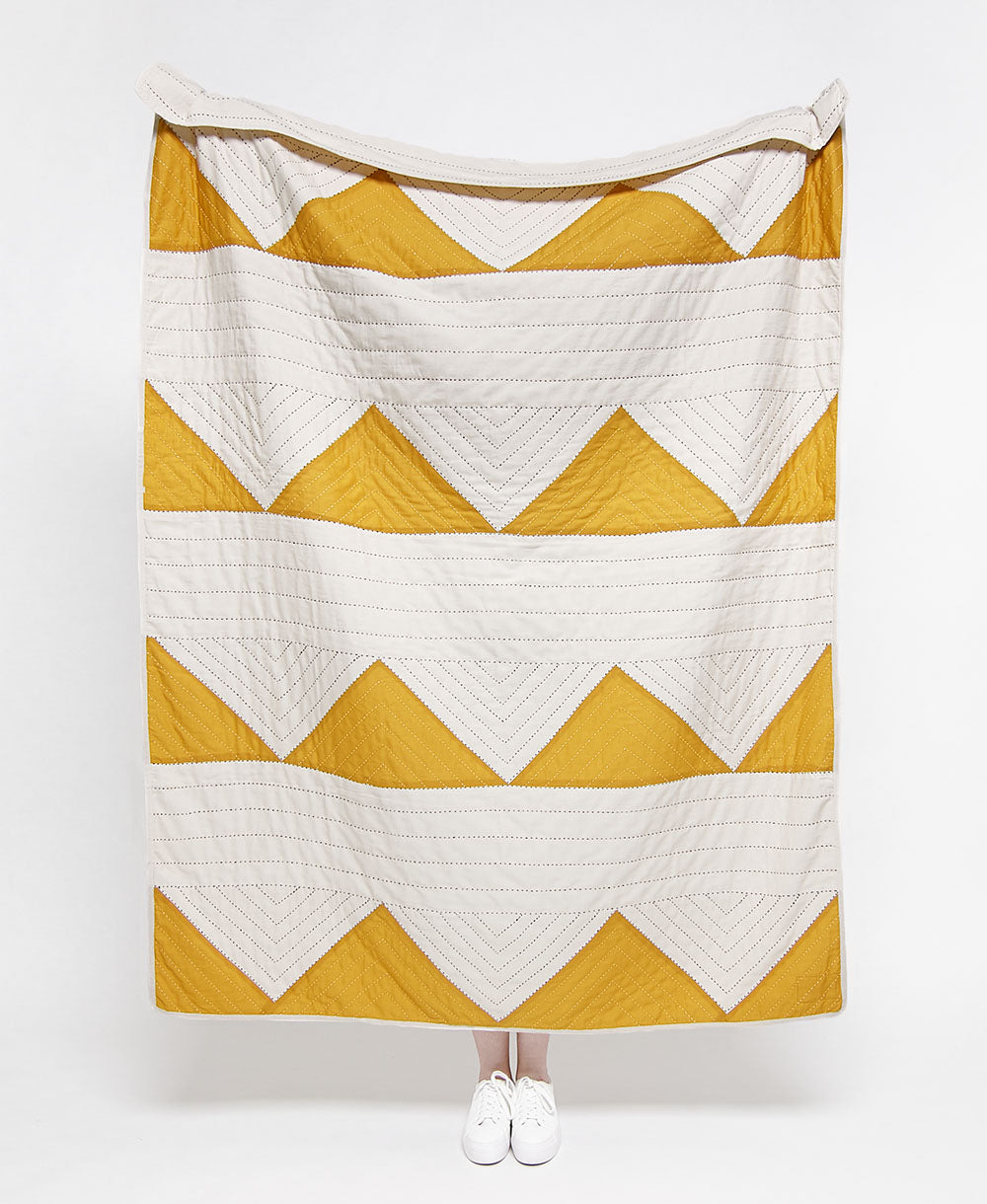 Yellow and white chevron patterned quilt on a white background