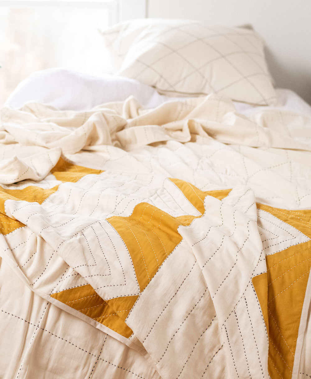 patchwork quilt with mustard yellow triangle pattern on all white bed