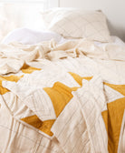 patchwork quilt with mustard yellow triangle pattern on all white bed