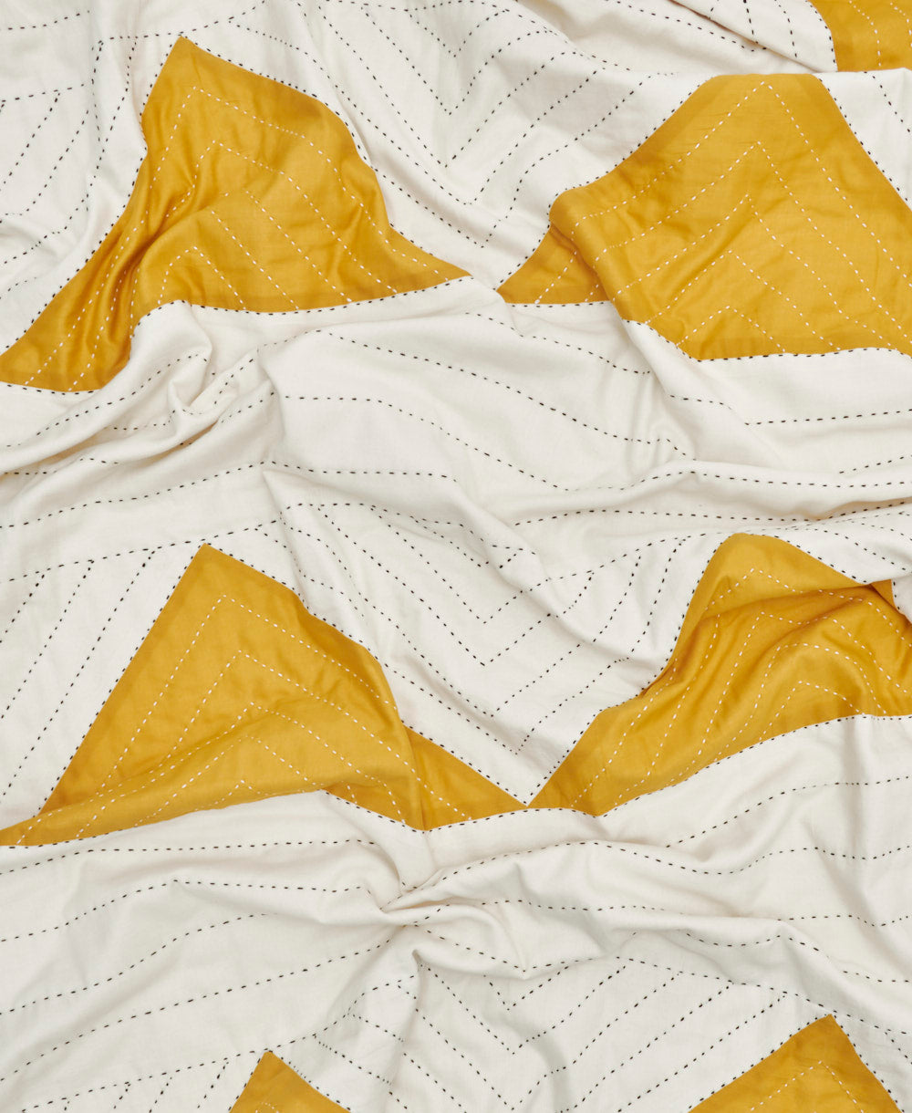 mustard yellow contemporary patchwork quilt in a triangle pattern with black hand-stitched embroidery