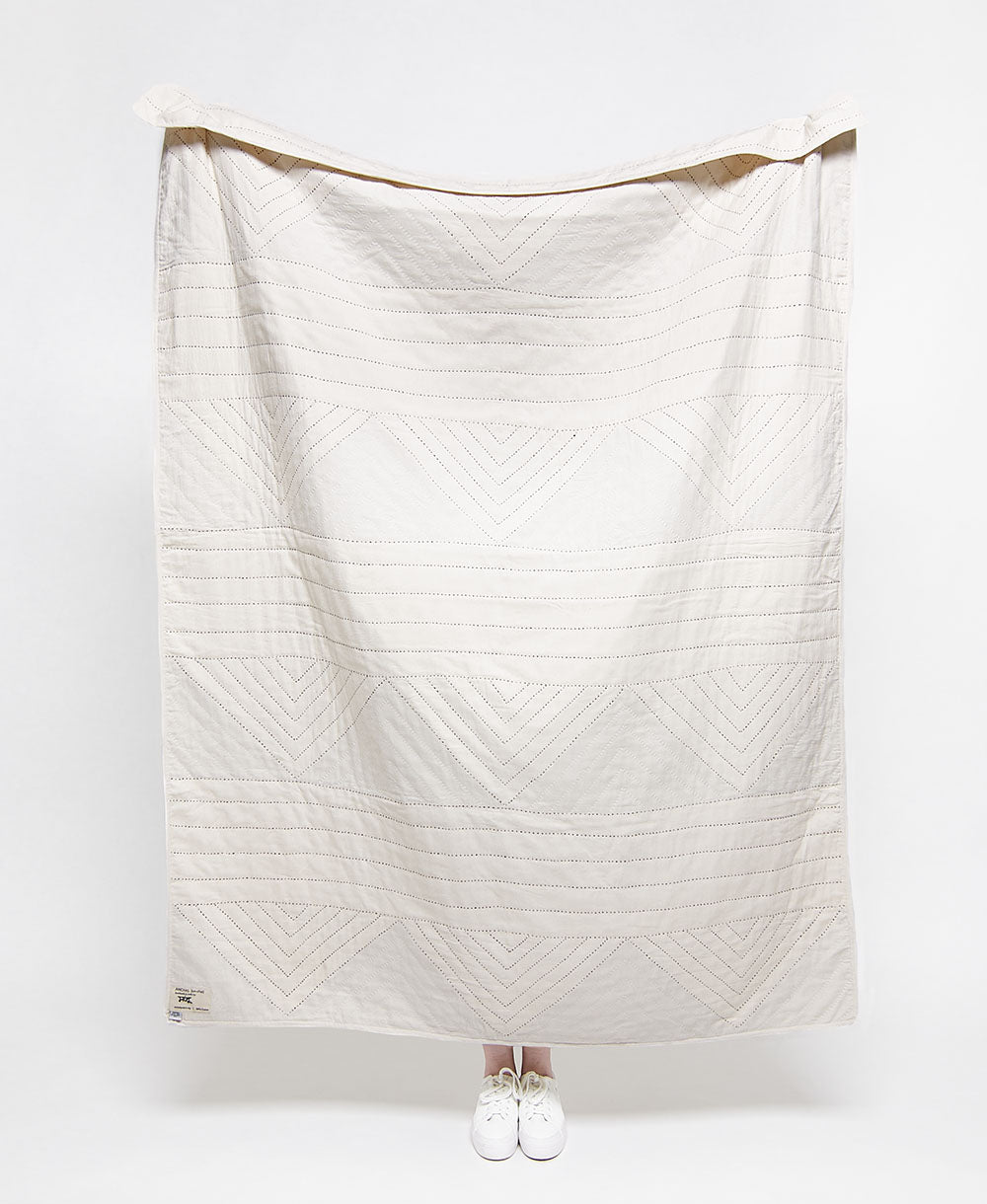 White quilt with a geometric pattern draped over a white background