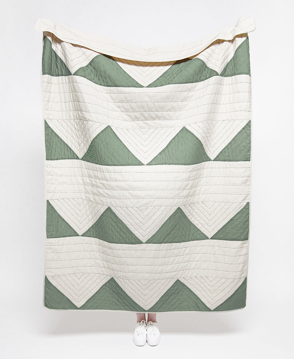 Green and white chevron patterned quilt draped over a person on a white background