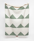 Green and white chevron patterned quilt draped over a person on a white background