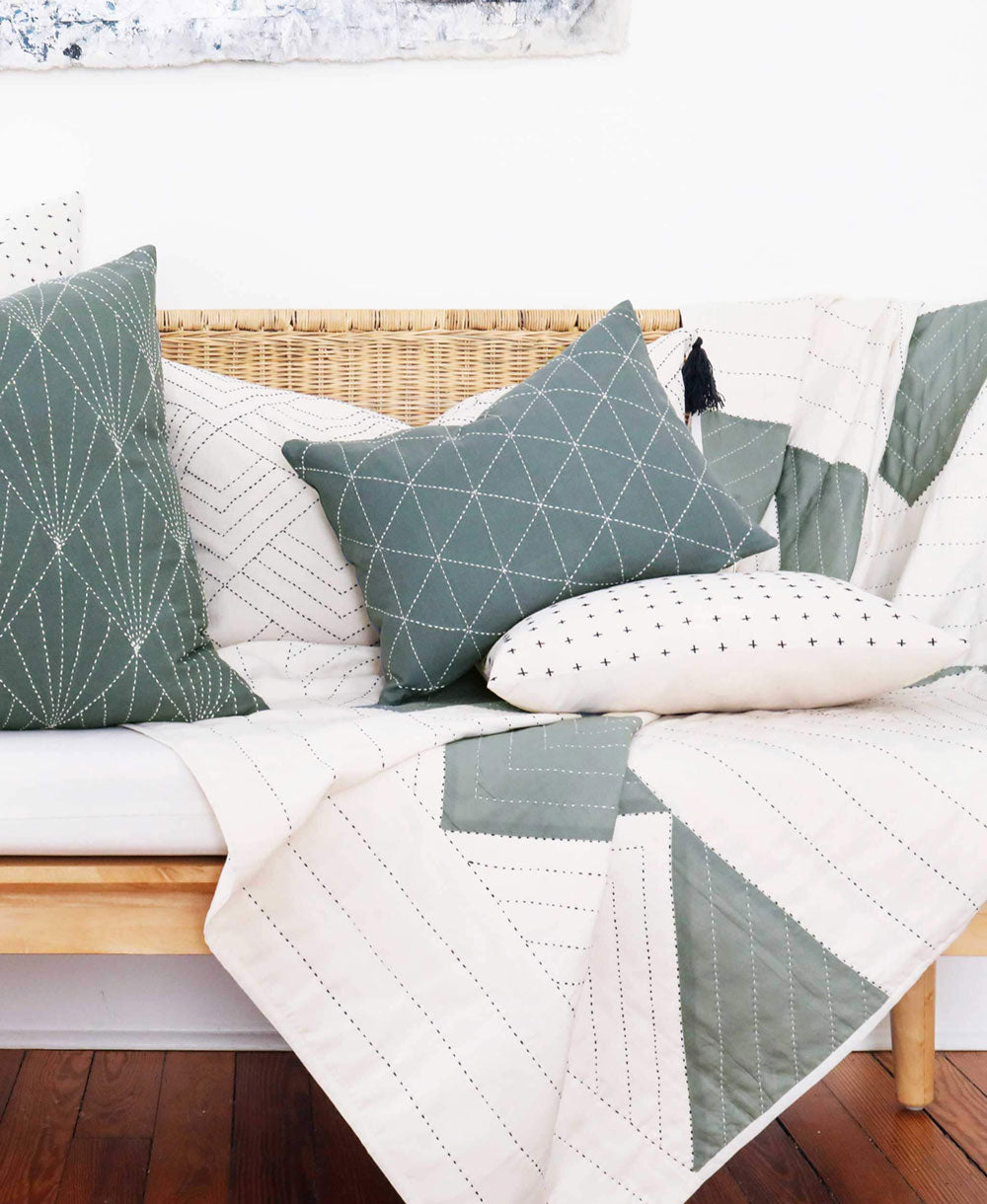 Sofa with geometric-patterned cushions and a matching quilt on a wooden floor.