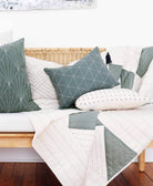 Sofa with geometric-patterned cushions and a matching quilt on a wooden floor.