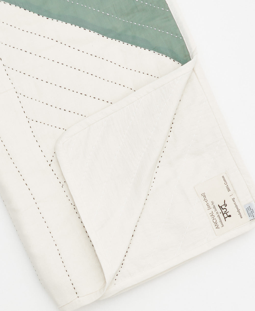 spruce green triangle patchwork quilt folded showing artisan signed tag on edge of quilt