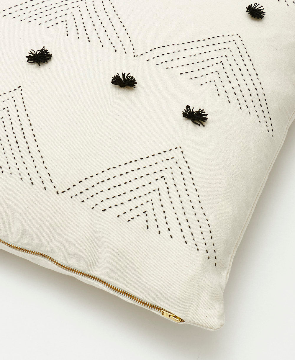 Decorative pillow with black embroidery and pom pom embellishments on a white background