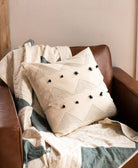 Decorative pillow with black pom-poms on a brown leather chair with a blanket