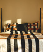 Bed with striped bedding and patterned pillows against a beige wall