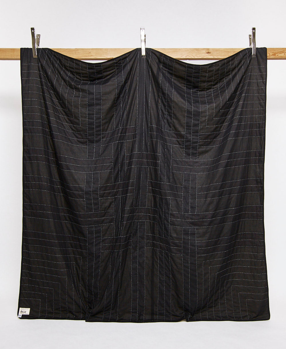back of woven patchwork quilt in solid black with white embroidery hanging on a wooden board with silver clips