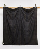 back of woven patchwork quilt in solid black with white embroidery hanging on a wooden board with silver clips