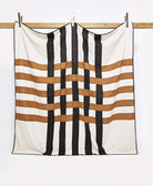 woven patchwork quilt in black, white, and camel hanging on wooden board with silver clips
