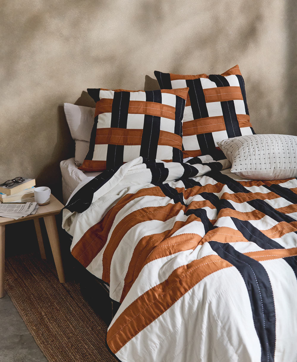 modern bed with geometric plaid bedding and checkered pillows against a beige wall