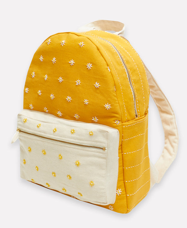 bright yellow cotton backpack with white straps and pockets covered in small hand stitched daisies