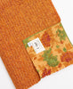 orange Kantha quilt throw with a tag featuring the hand stitched signature of the maker