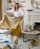 Woman draping a yellow throw blanket over a couch 