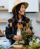 woman smiling in straw sunhat making floral arrangement in quilted plaid chore jacket made from organic cotton