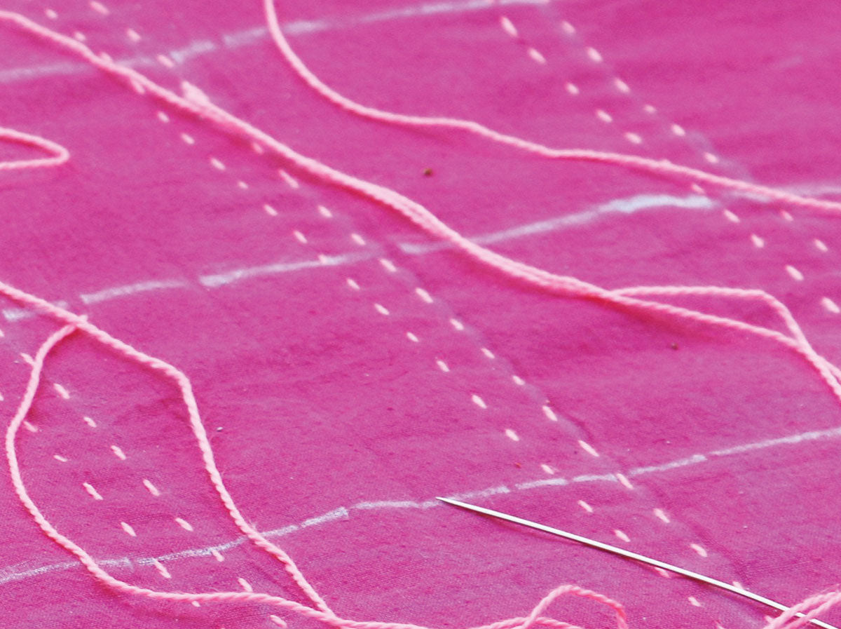 Close up of needle and pink thread sewing a pattern into magenta fabric