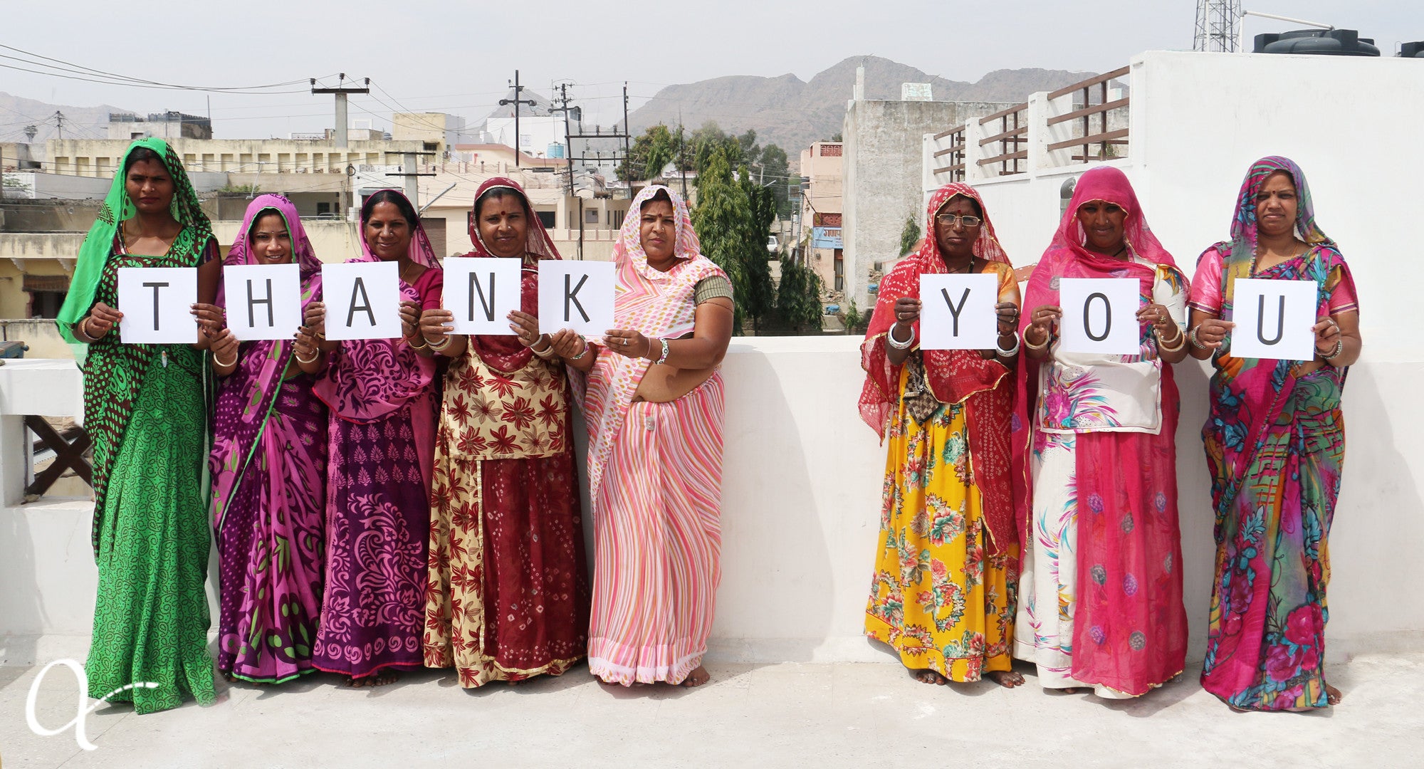 Eight artisan women standing in a line, each one holding up a letter to spell thank you in celebration of Anchal's gracious donors