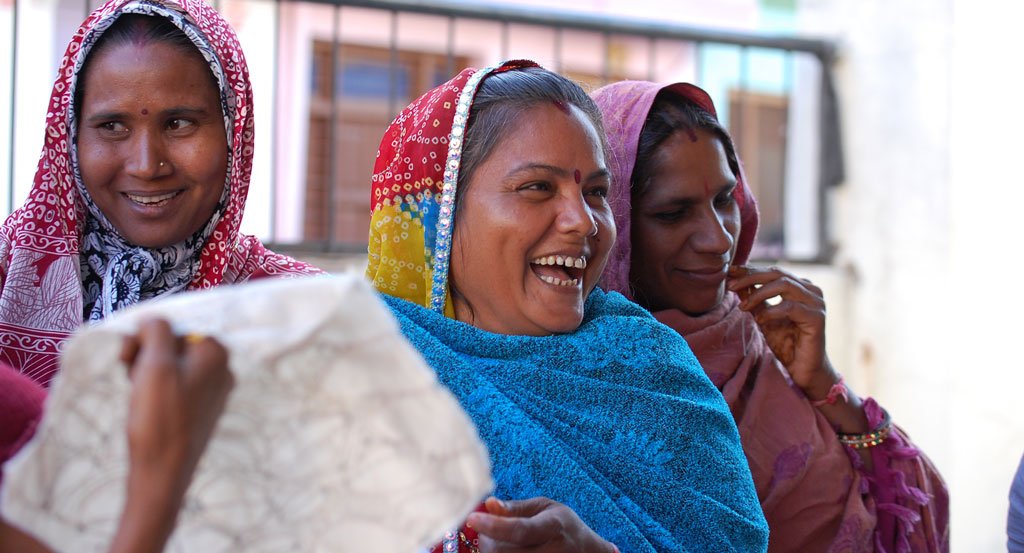 Three artisan women laughing with joyful expressions excited to greet the Anchal team 