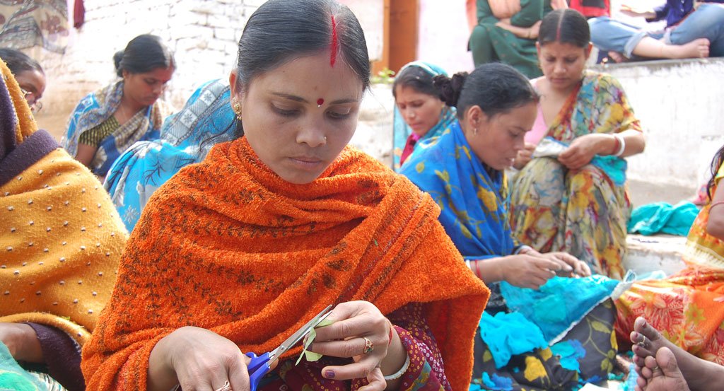 Artisan woman using scissors to cut a small piece of fabric for a project at an Anchal workshop 