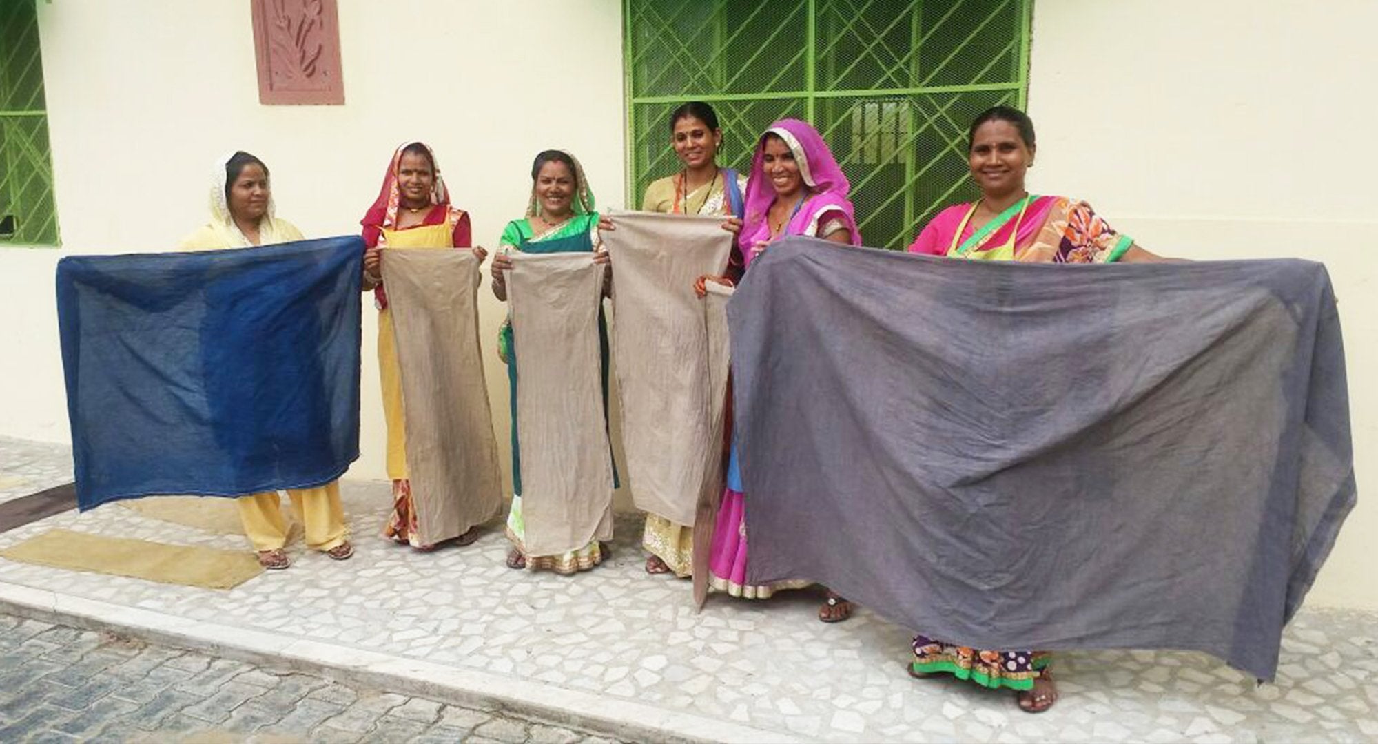 Six Anchal artisan women each holding up naturally dyed fabric from the project Designing colorful change, provided by the grant from Dining for Women 