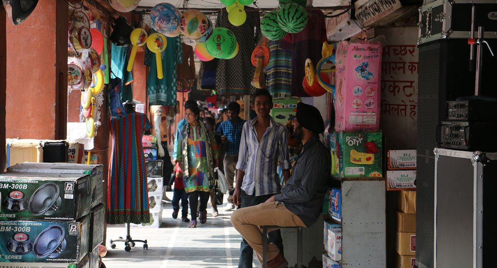 Corridor of an Indian marketplace filled with lanterns, Indian goods, and people