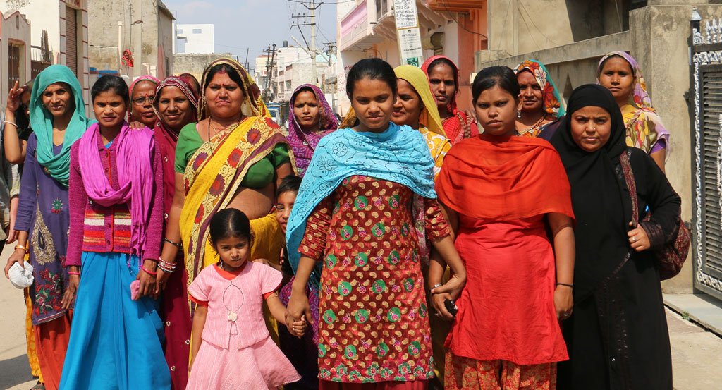 Large group of Indian women dressed in Sari's holding hands walking down the street