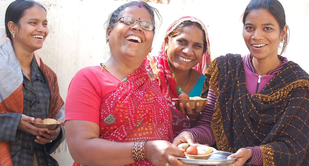alt="Four Indian women gathered, laughing and smiling joyfully"