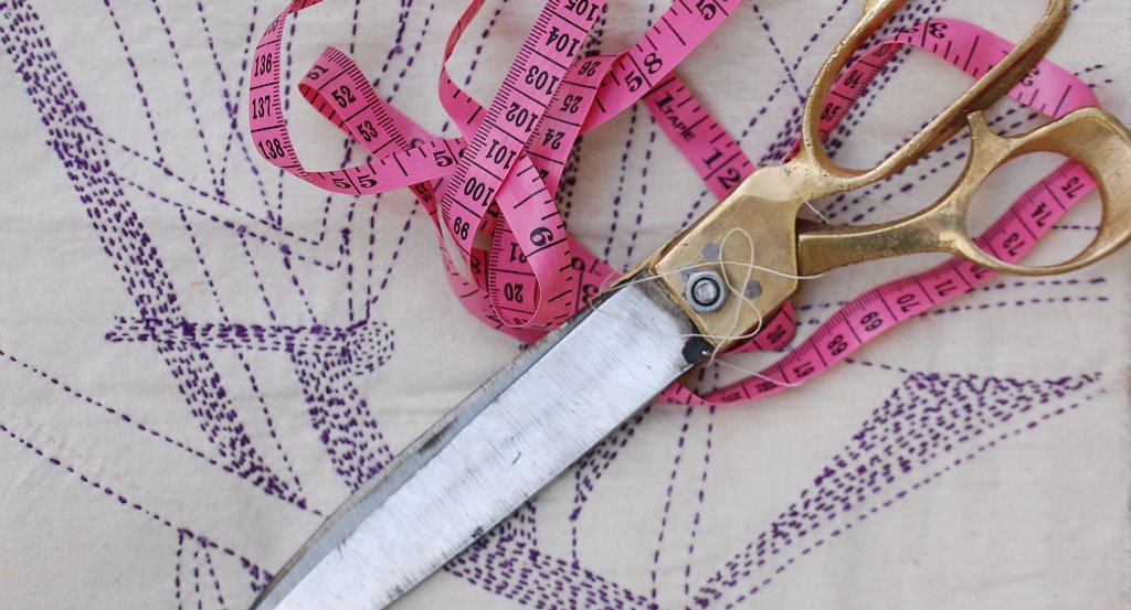 Scissors and a tape measure laying on top of an hand stitched design pattern 