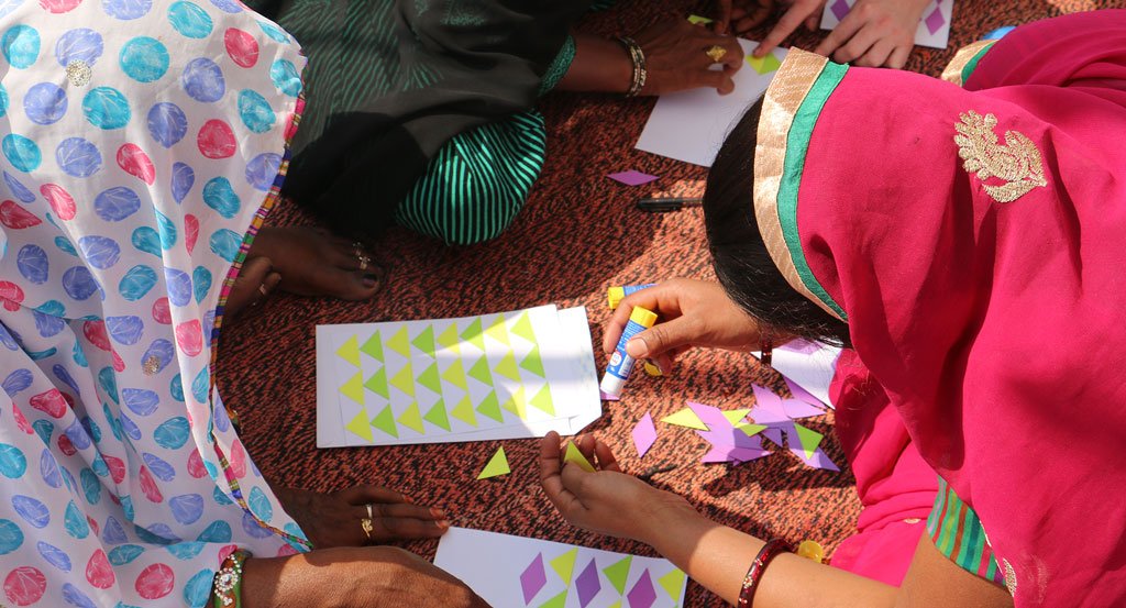 Two artisans creating triangle patterned art work by using small colored paper and glue