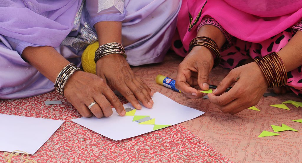 Anchal artisans glueing together colorful yellow pieces on paper to help spark inspiration for innovative new design patterns