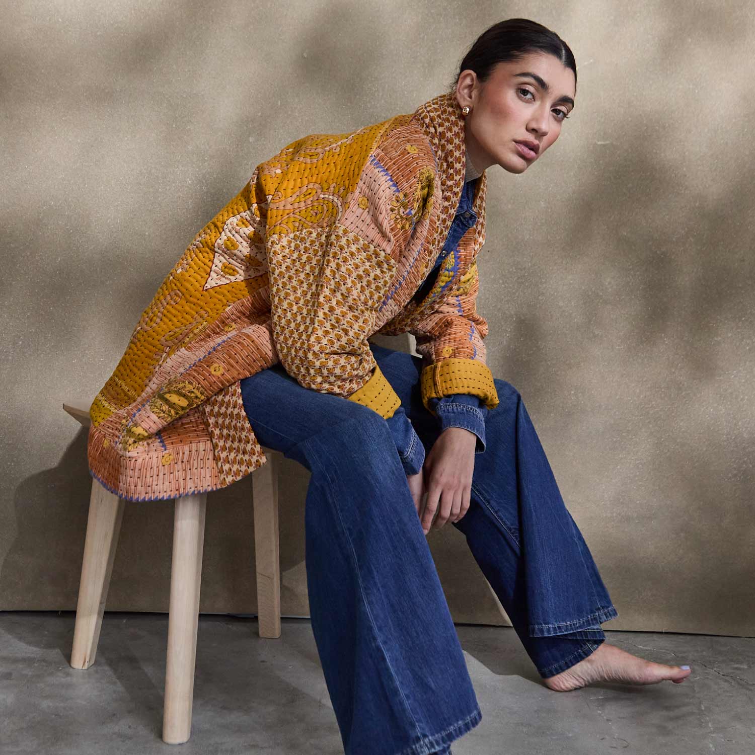 woman sitting on light wooden stool wearing orange quilted jacket made from one-of-a-kind vintage saris