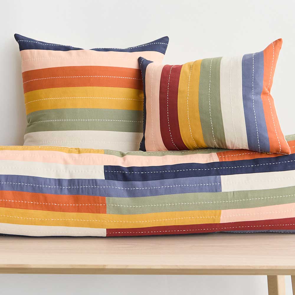 colorful rainbow striped throw pillows made from 100% organic cotton in India sitting on wooden bench