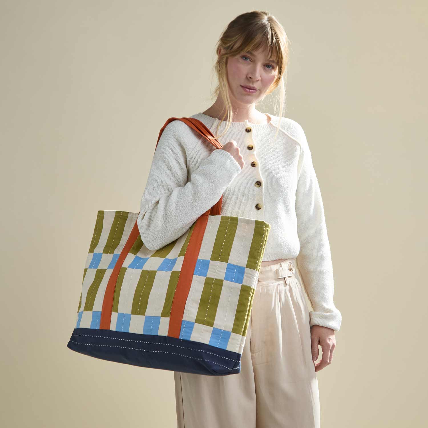 woman carrying large canvas tote bag over her shoulder in olive green, sky blue, and orange