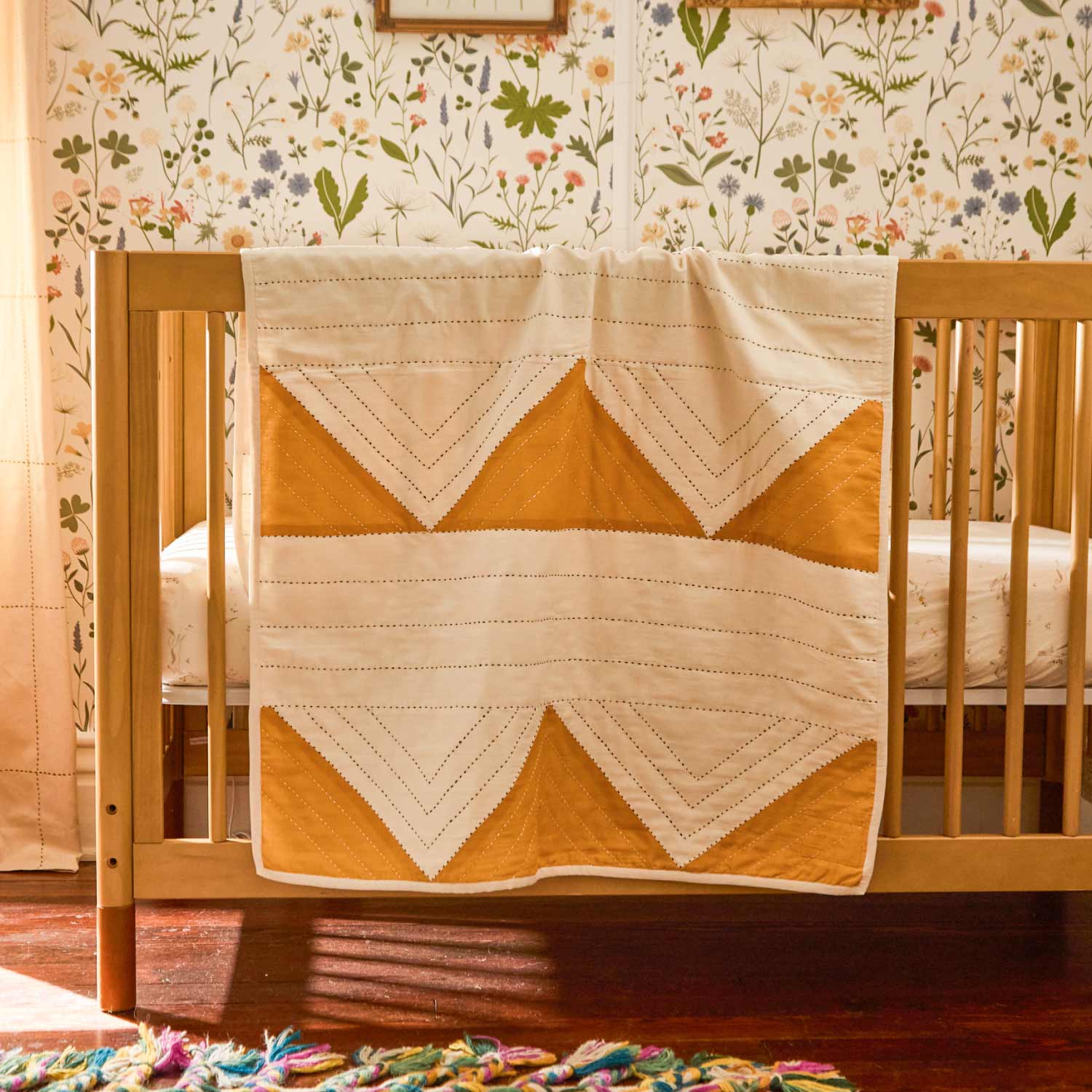 geometric quilted baby blanket draped over wooden crib