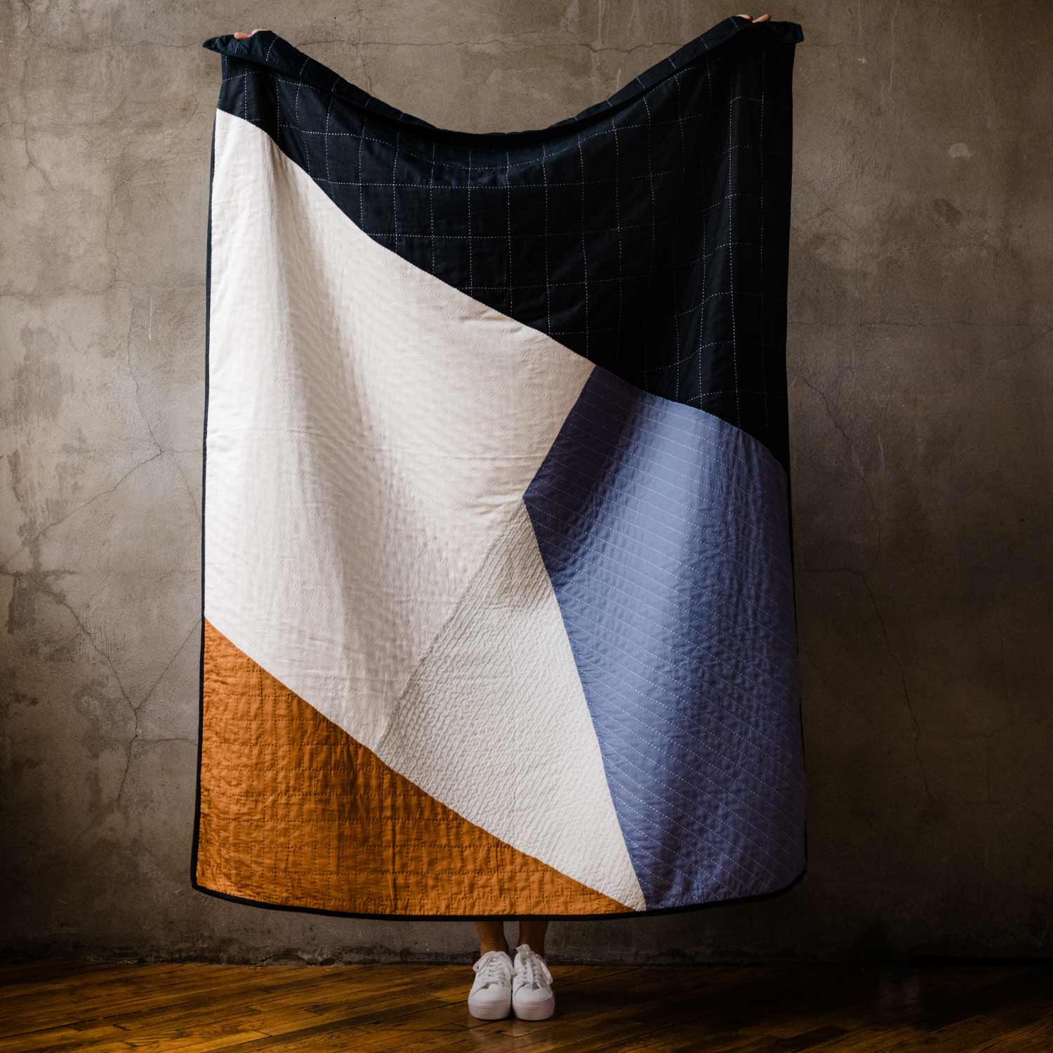 woman holding up modern patchwork quilt in angular geometric design made in India