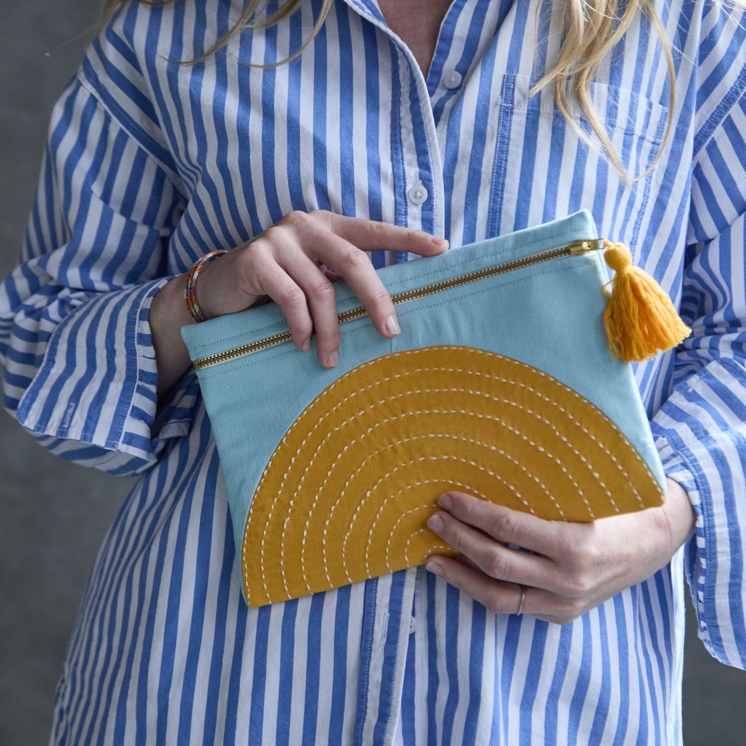 woman holding embroidered pouch bag in sky blue and mustard yellow in eclipse design