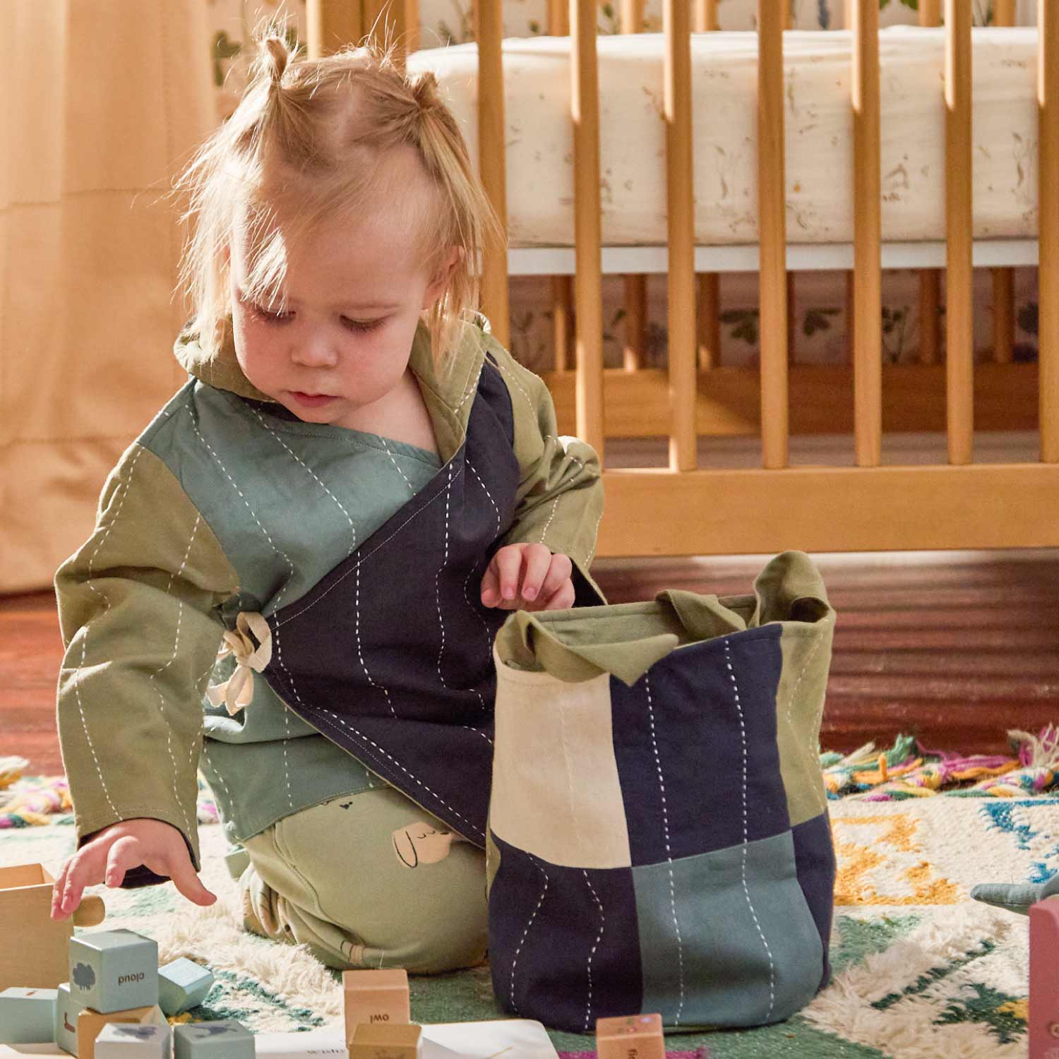 toddler girl putting wooden blocks into fabric basket in checkered green and blue print