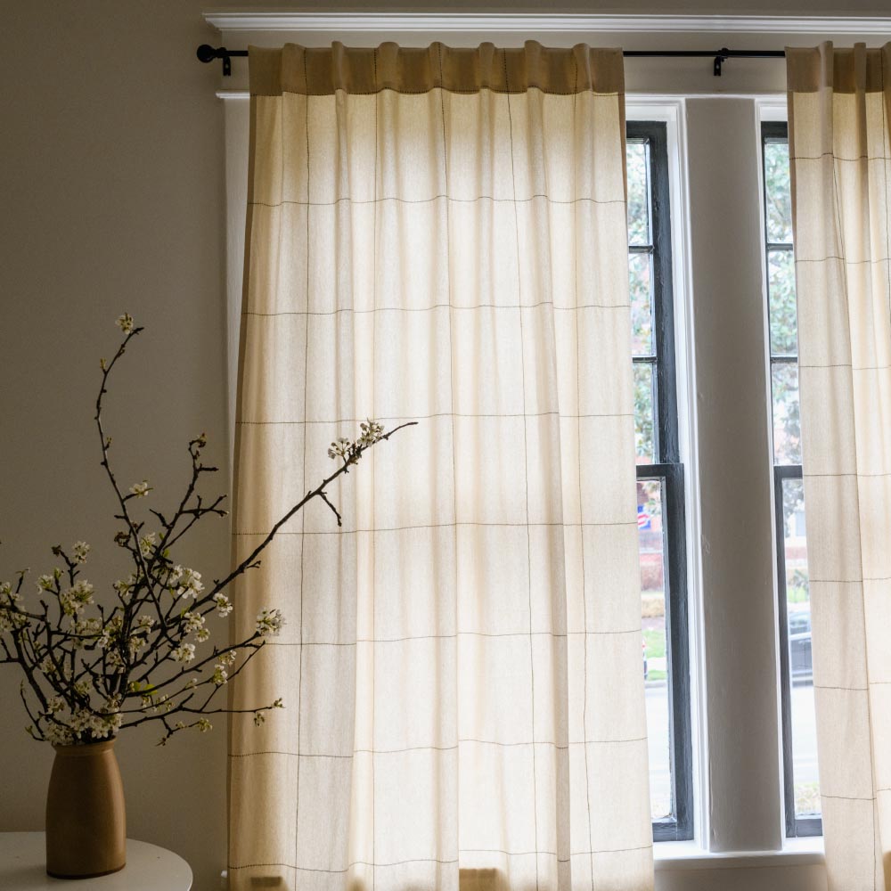 off-white light filtering curtains hanging on black curtain rod with large grid-stitch embroidery