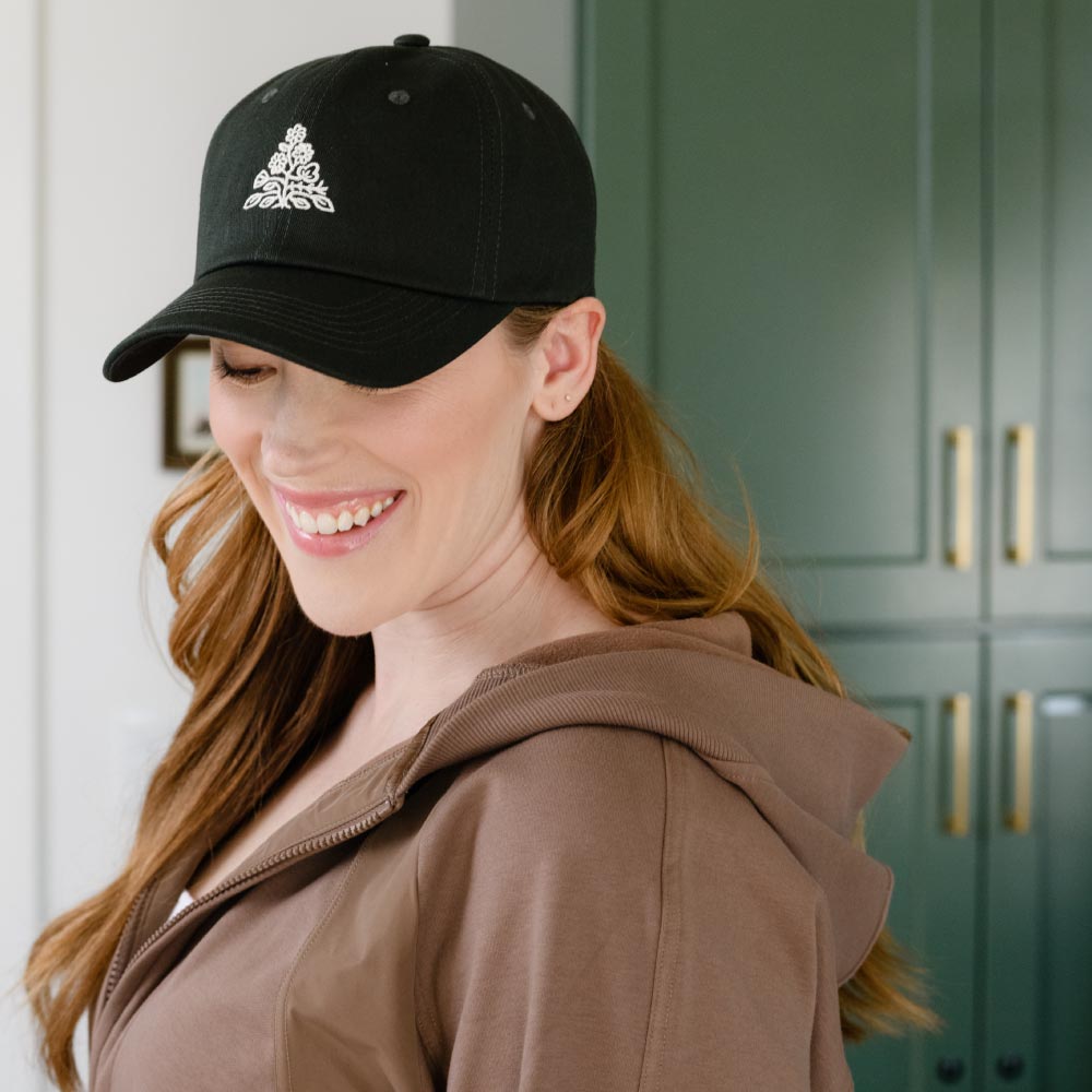 woman wearing hunter green baseball cap with cream embroidered logo mark on the front by Anchal