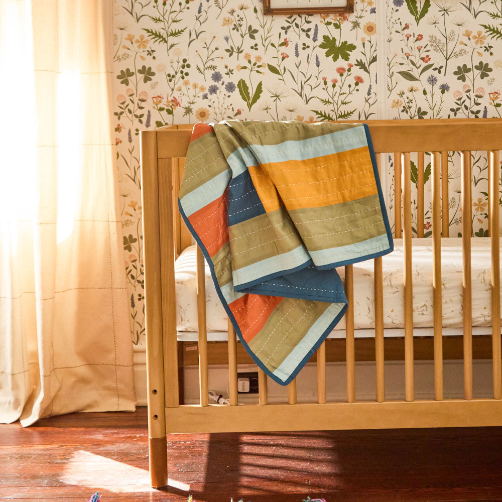 small modern kantha quilt in a colorful geometric stripe pattern draped over modern wooden crib